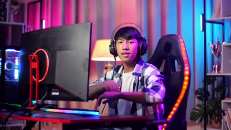 asian teen boy gamer smiling to camera with crossed arms while playing video game on computer
