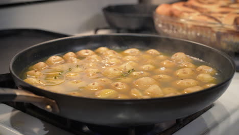una sartén de hierro caliente en la estufa llena de papas hirviendo y humeando a cámara lenta