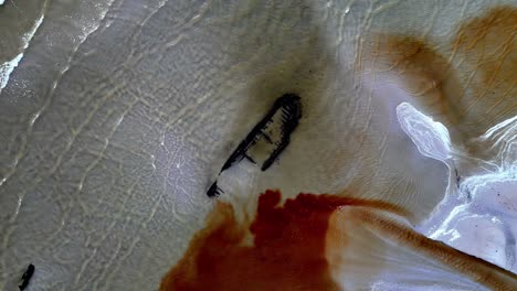 old shipwreck on a sandy beach with clear blue water, taken from a drone directly above old ship an eco-catastrophe is forming, a dark liquid is flowing into the ocean