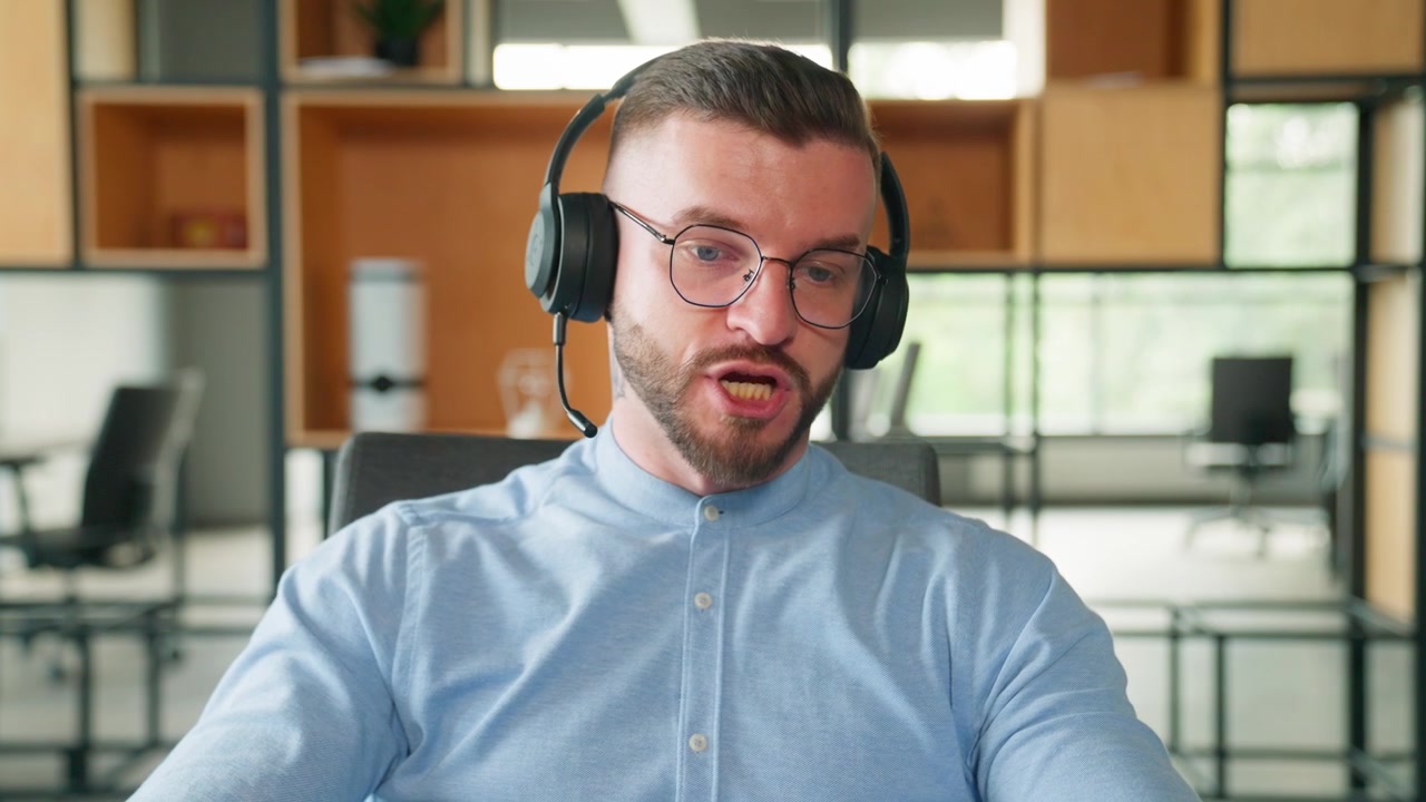 Giovane uomo barbuto con le cuffie che parla in videochiamata in ufficio