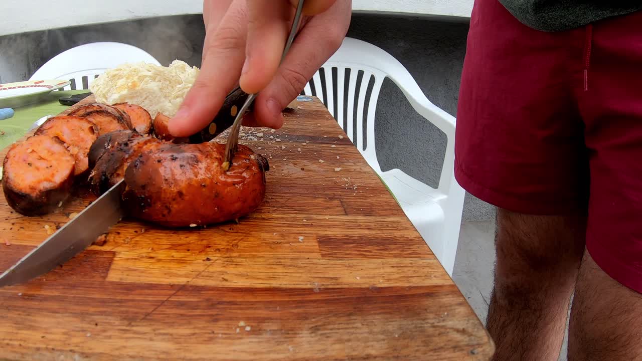 Slow motion video of a white man cutting a sausage on a wooden board