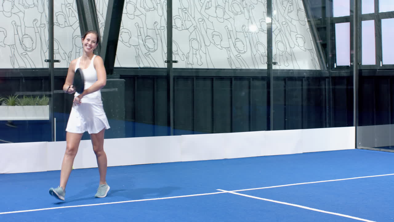 Woman in white dress playing padel tennis with partner on indoor court