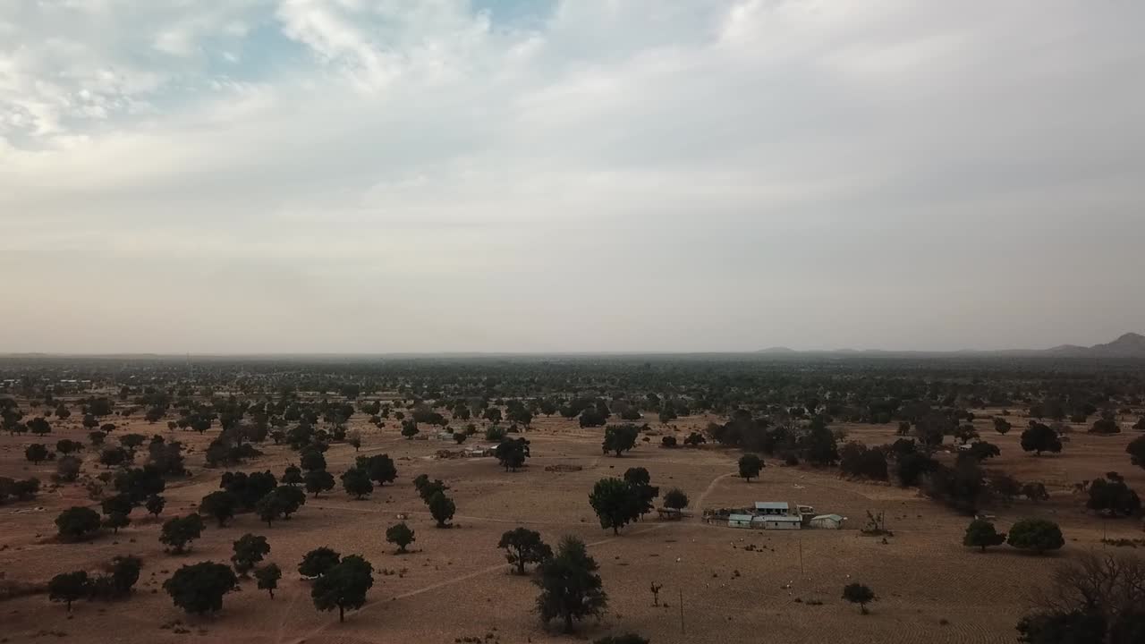 Wide aerial panorama of Northern Ghana's flat savannah landscape dotted with scattered Shea trees and rural settlements under a hazy sky
