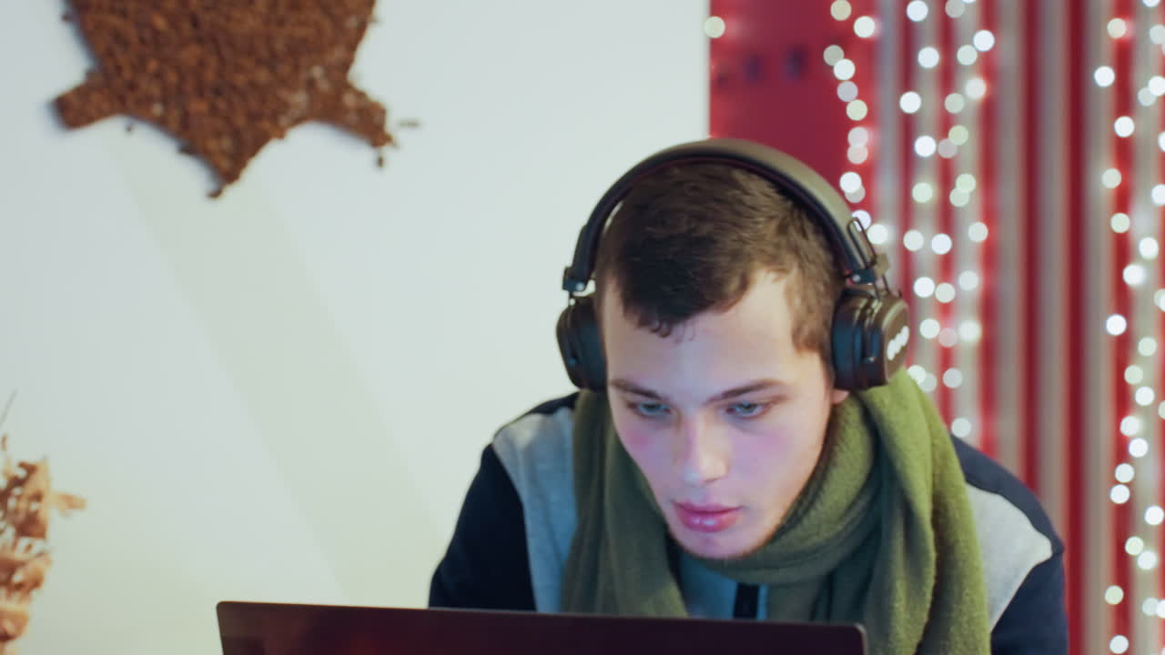 Young caucasian man debugging code on laptop, headphones and green scarf, fairy lights backdrop, intense screen glow, close up concentration, remote workspace and software testing
