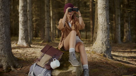 female explorer looking through binoculars in forest