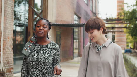 two multiethnic girlfriends walking with shopping bags on street