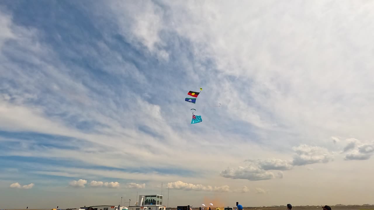 Parachutists descend with flags under a vibrant sky during the Avalon Airshow in Geelong, showcasing dynamic aerial maneuvers