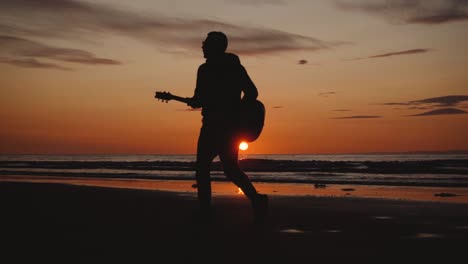 man running with guitar in back sand beach at sunset