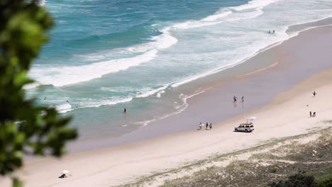 people and vehicles on a sunny beach with waves