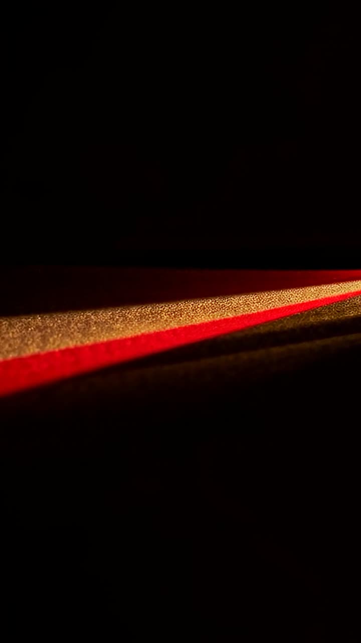 Video verticale: proiezione di una luce calda che si sposta su una striscia dorata, bordo rosso in una stanza buia, da cambio camera