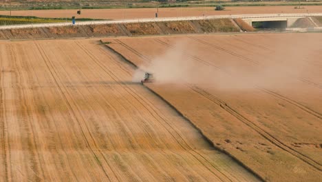 Combine-harvester-harvesting-cereals-on-a-sunny-summer-day,-dust-rising,-aerial-close-up-shot