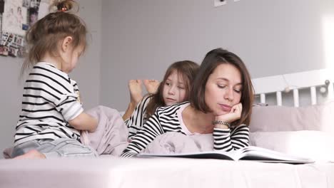 Mother-is-reading-a-book-for-her-two-daughters-lying-on-a-bed.-Identical-clothes