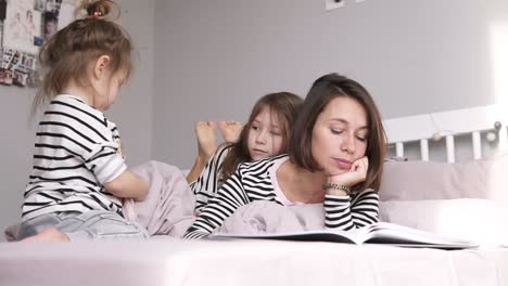 mother is reading a book for her two daughters lying on a bed. identical clothes