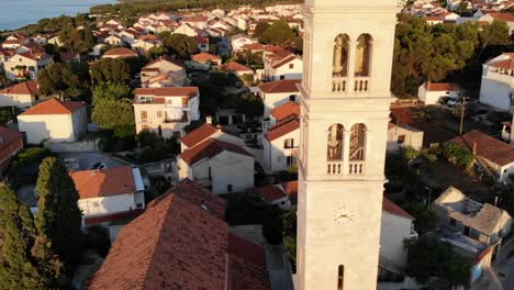 a drone shot of a church and a belltower in supetar, the island of brac, croatia