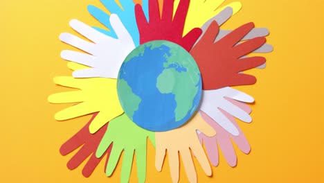 close up of hands together with globe made of colourful paper on yellow background with copy space