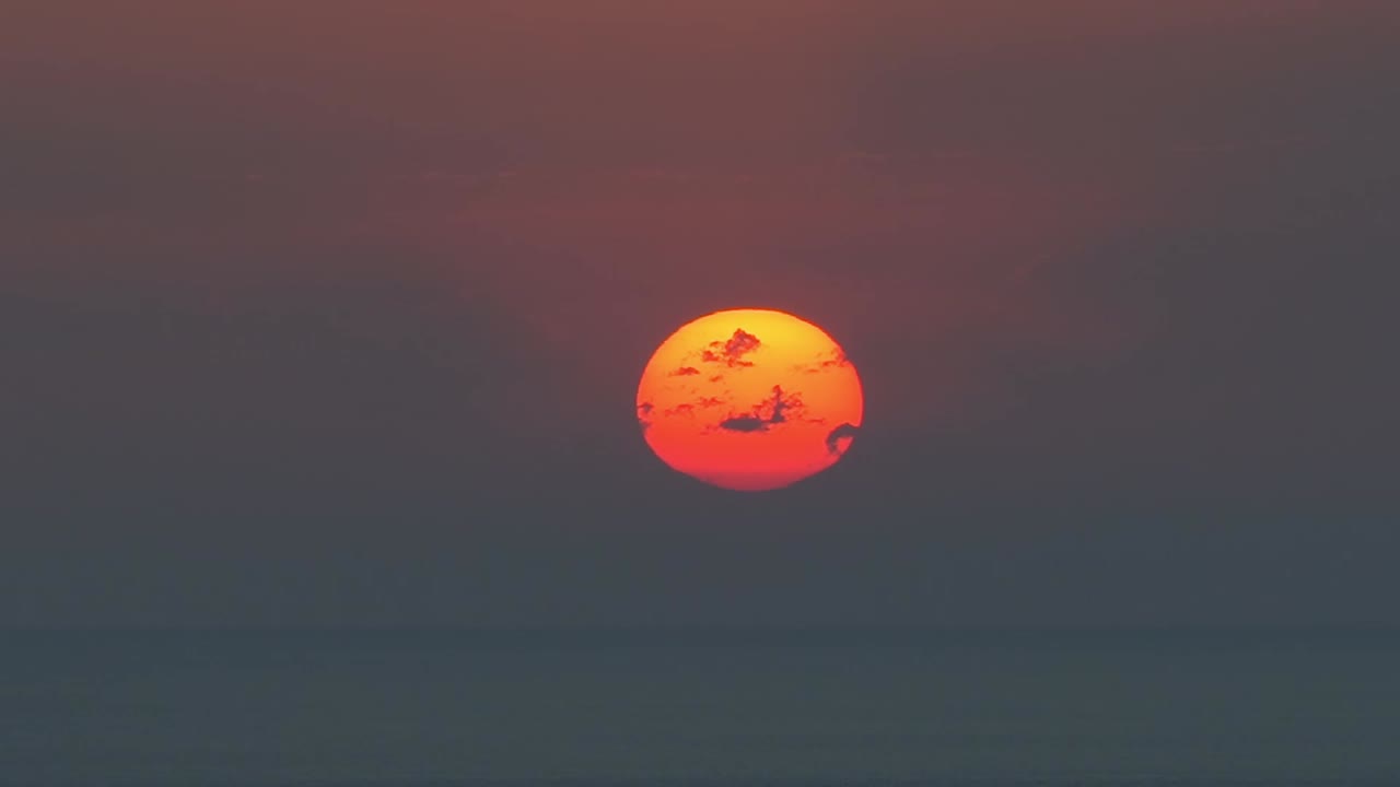 Close-up of the setting sun, glowing orange before disappearing over the horizon.