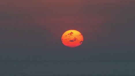 un primer plano del sol poniéndose, brillando de color naranja antes de desaparecer sobre el horizonte.