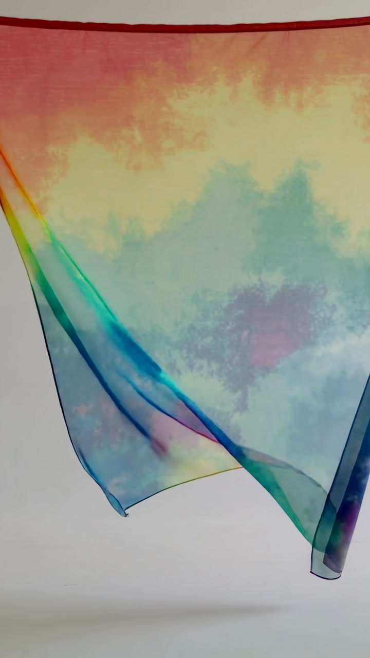 Vertical video: Entering from right, tie-dye scarf billowing across studio wall, red hem, shadow