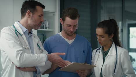 tres médicos caucásicos serios discutiendo sobre documentos en la clínica médica