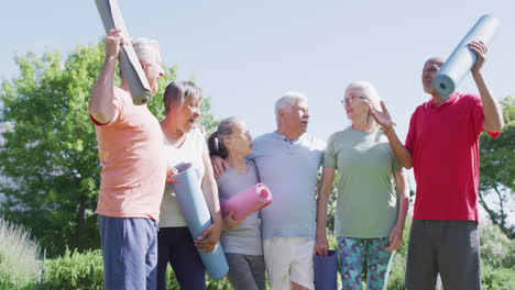 Diverse-group-of-happy-male-and-female-seniors-talking-after-exercising-in-sunny-garden,-slow-motion