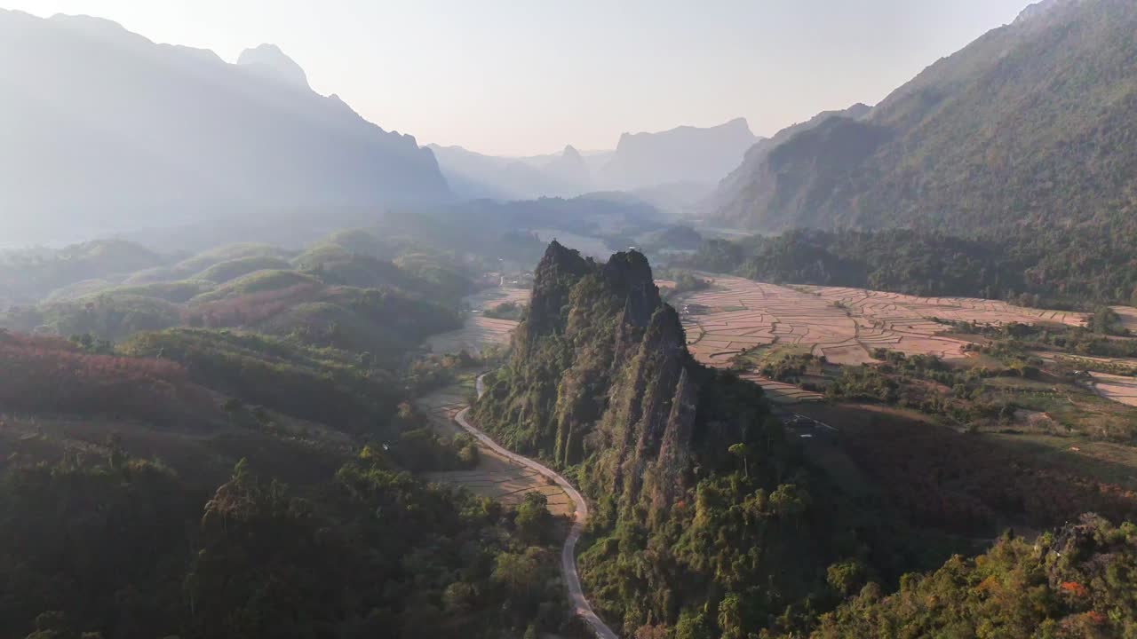 Spettacolari formazioni calcaree si ergono dal fondovalle a Nam Xay, Vang Vieng, Laos, circondate da dolci colline, terreni agricoli e una tortuosa strada rurale nella morbida luce del mattino o della sera