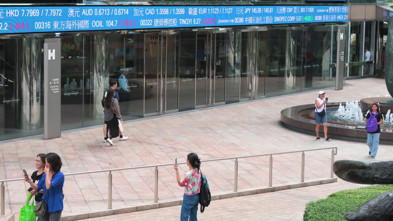 People take photos with a moving screen in the background displaying negative stock ticker symbols at Exchange Square, home to the Hong Kong Stock Exchange (HKEX), in Hong Kong's financial district.