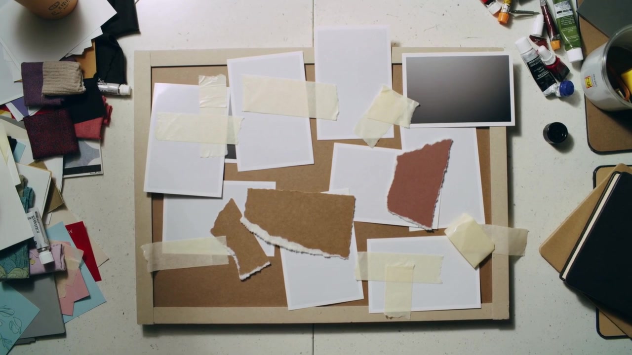 Falling white cards landing on framed corkboard at tabletop, forming collage with masking tape