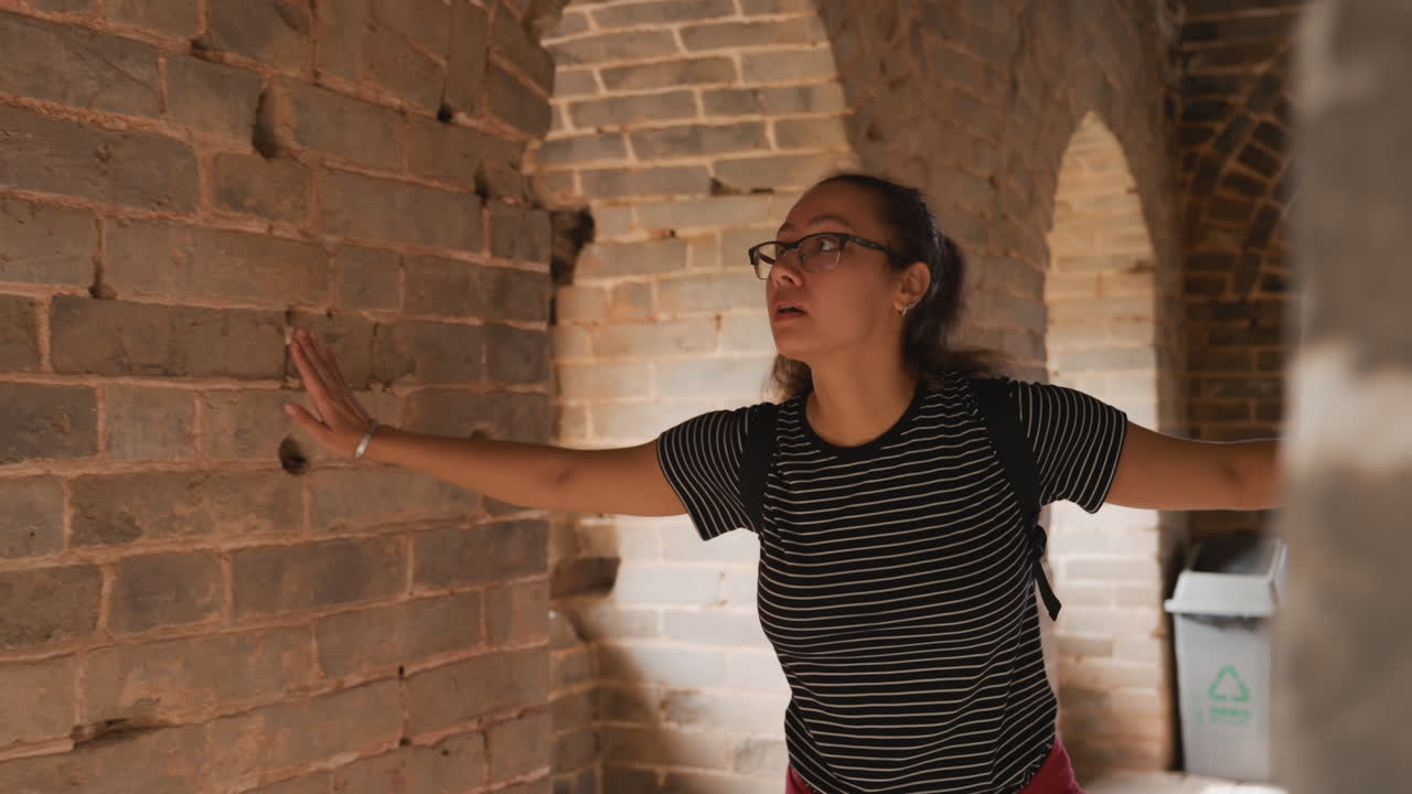 Estudante inspeciona cuidadosamente um arco de tijolos. Jovem com óculos estuda atentamente uma passagem histórica de tijolos. Jovem revisa notas detalhadas sobre um arco antigo de tijolos com foco.