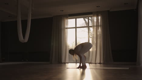 Lens-flare-:A-young-woman-in-white-sportswear-is-stretching-with-a-large-hall-with-large-windows-in-a-slow-motion-scheme-the-sun's-rays-shine-through-the-window.-Healthy-lifestyle-healthy-morning