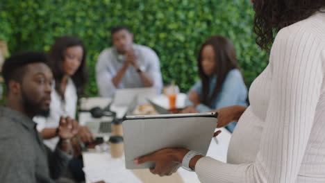 Afroamerikanische-Geschäftsleute-Treffen-Schwangere-Teamleiterin,-Die-Einen-Tablet-Computer-Nutzt,-Um-Das-Design-Mobiler-Anwendungen-Zu-Präsentieren-Und-Kreative-Ideen-Für-Die-Kommunikations-App-In-Einer-Büropräsentation-Auszutauschen