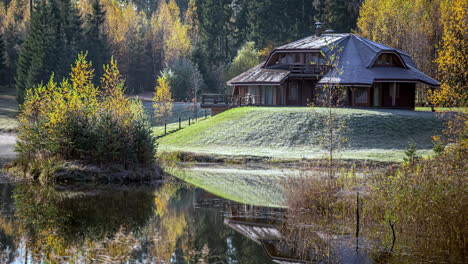 cottage by a river in autumn with fall colors, and frost on the grass - time lapse