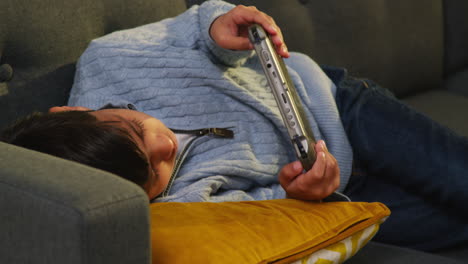 young boy lying on sofa at home playing game or streaming onto handheld gaming device 2