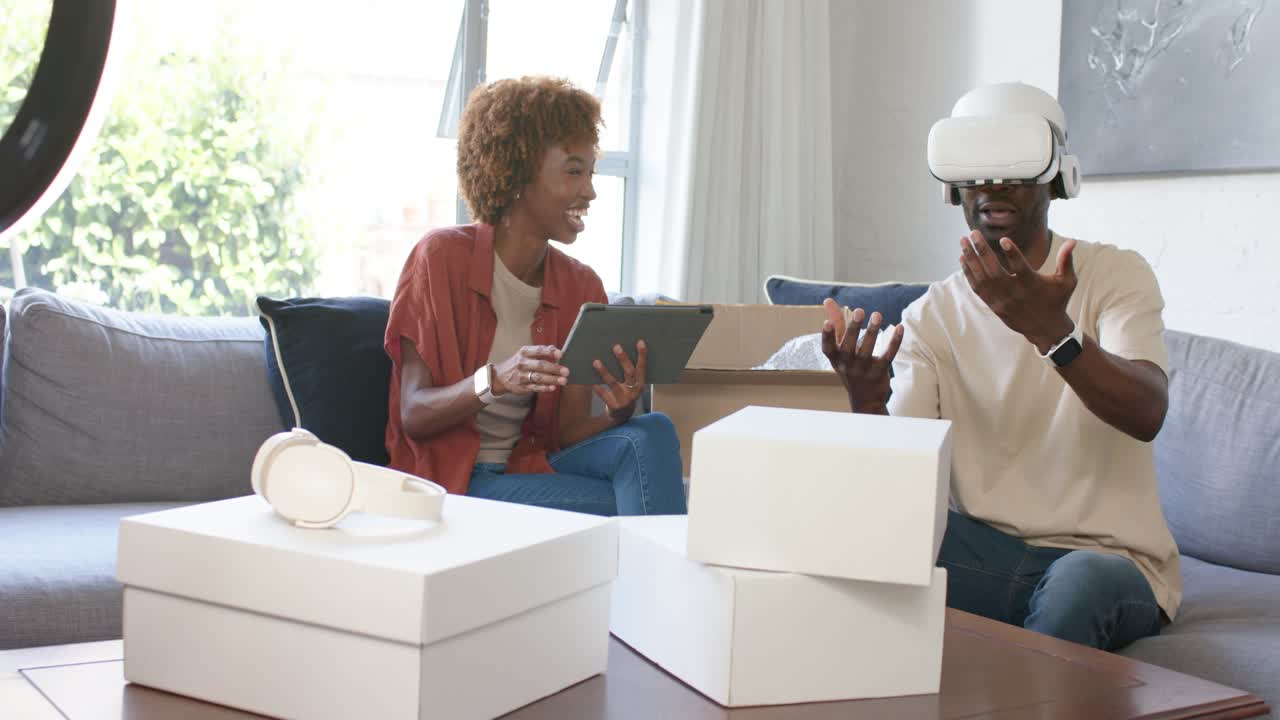 African American couple unboxing and testing white VR headset at home, woman holding tablet guiding