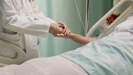 Médico-Sosteniendo-La-Mano-De-Una-Anciana-En-La-Cama-De-Un-Hospital-Reconfortando-A-Un-Paciente-Anciano-Hospitalizado-Recuperándose-De-Una-Enfermedad-Profesional-Médico-Al-Lado-De-La-Cama-Dando-Aliento-Y-Apoyo-A-La-Atención-Médica