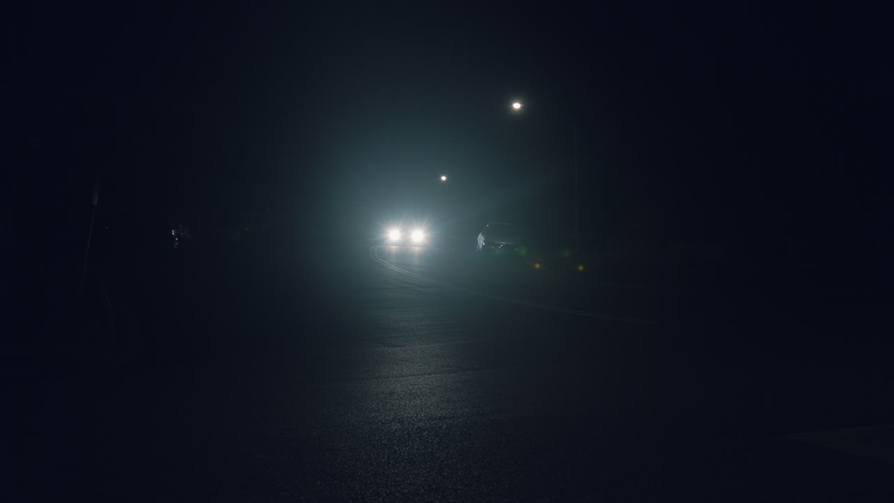 Headlights Of An Approaching Vehicle Traveling On A Dark Asphalt Road. - Tracking Shot