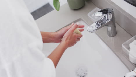 Midsection-of-biracial-woman-washing-hands-in-bathroom,-slow-motion