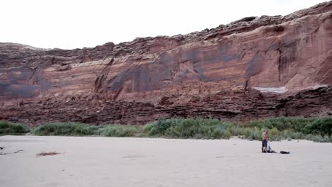 Pan-of-guy-setting-up-tent-on-beach-in-Utah-canyon