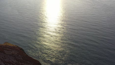 Drone-shot-tilting-up-while-looking-at-the-refection-of-sun-rays-on-the-ocean-from-sunset-on-the-North-Devon-coast-in-the-UK