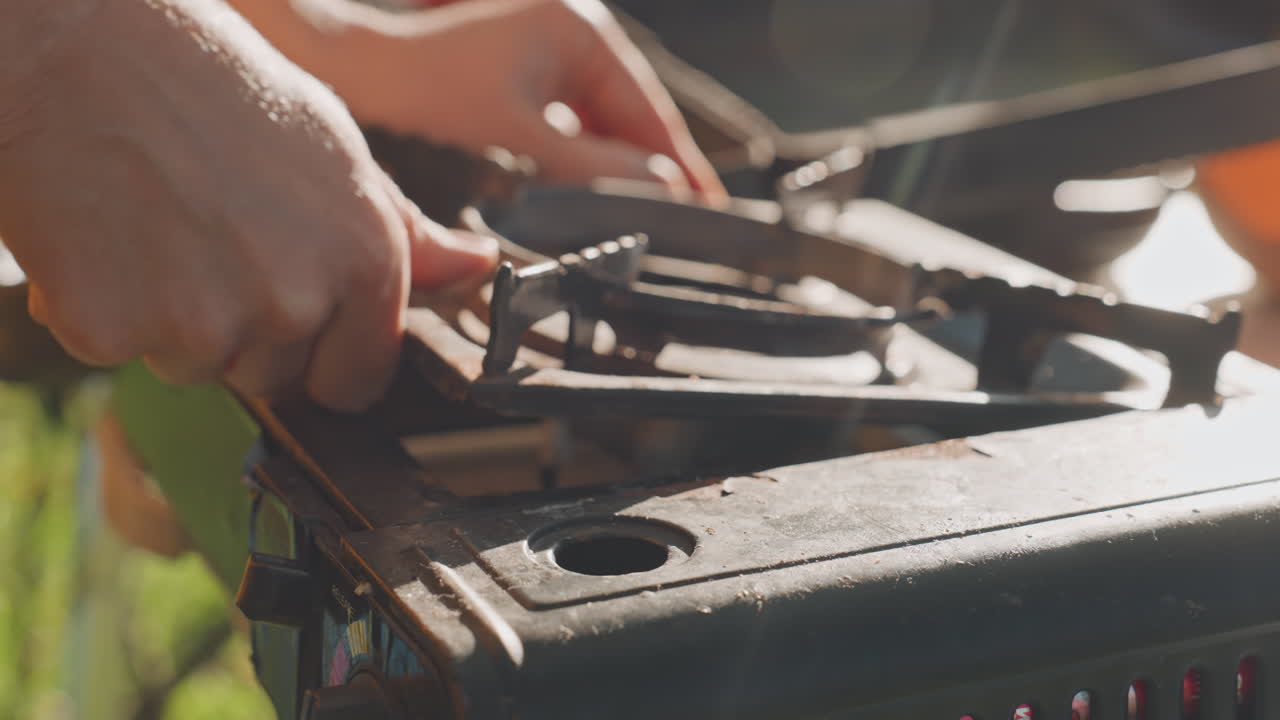 Hands assembling camping stove outdoors carefully. Quiet work fitting metal parts on camping stove in forest. Close examination of hands assembling stove components in sunlit natural setting