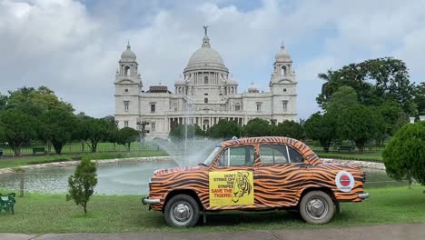 Shot-of-yellow-taxi-with-black-stripes,-advertising-tiger-conservation-standing-in-front-of-Victoria-Memorial-in-Kolkata,-India-on-a-cloudy-day