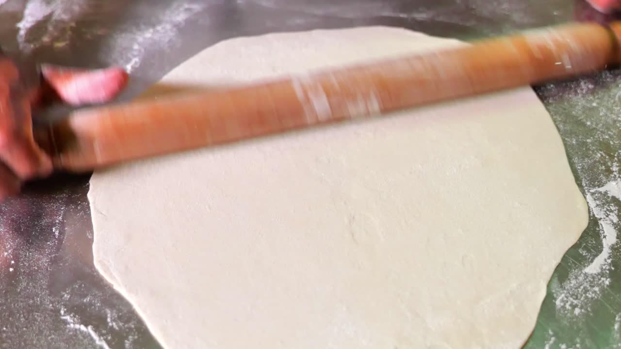 persona extendiendo masa de pizza usando un rodillo en una barra de acero inoxidable