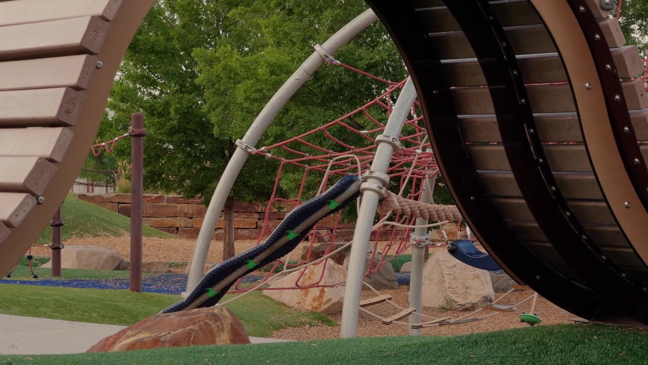 Right to left glide hides a playground climbing structure behind foreground blur.