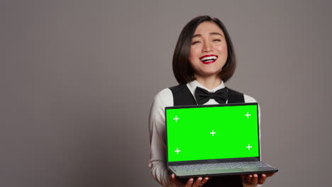 Asian-hotel-concierge-holding-pc-with-greenscreen-on-camera