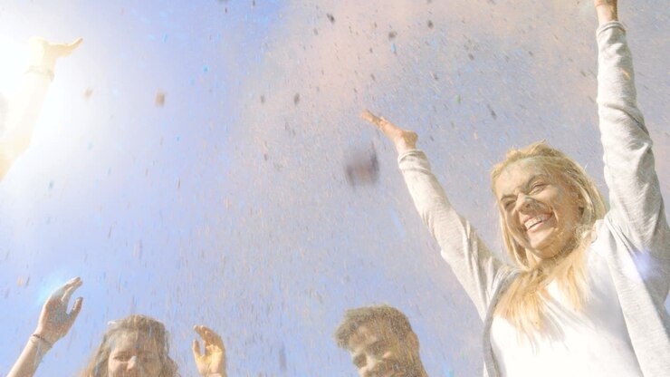 Low Angle Shot of Multi-Ethnic Group of Diverse Young People Dancing and Throwing Colorful Powder in the Air in Celebration of Holi Festival. They Have Enormous Fun on this Sunny Day.