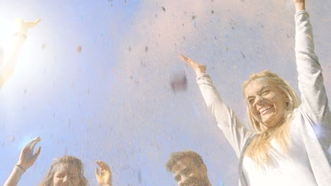 low angle shot of multi-ethnic group of diverse young people dancing and throwing colorful powder in the air in celebration of holi festival. they have enormous fun on this sunny day.