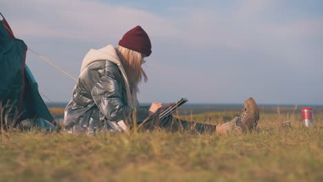 girl-in-warn-jacket-uses-tablet-at-tent-on-autumn-meadow