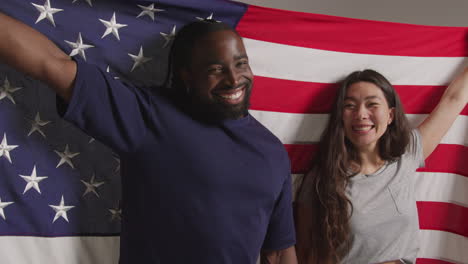 studio portrait shot of multi-cultural couple holding american flag behind them celebrating 4th july independence day 2