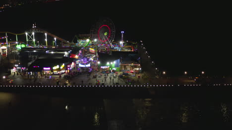 AERIAL:-Santa-Monica-Pier-at-night-with-Ferris-Wheel-and-colorful-lights,