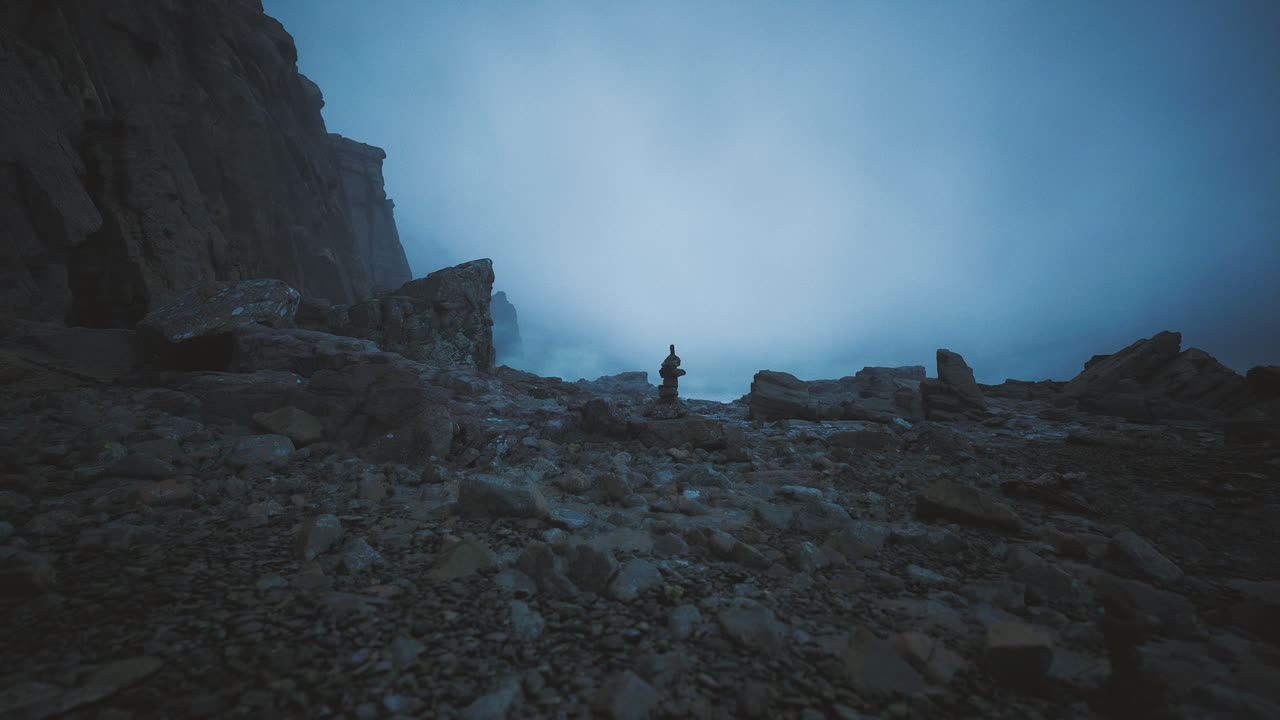 Mysterious figure stands among rocky terrain during foggy twilight hours