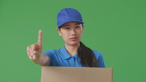 primer plano de una mensajera asiática en uniforme azul que no muestra ningún gesto mientras entrega una caja de cartón en el fondo de la pantalla verde en el estudio